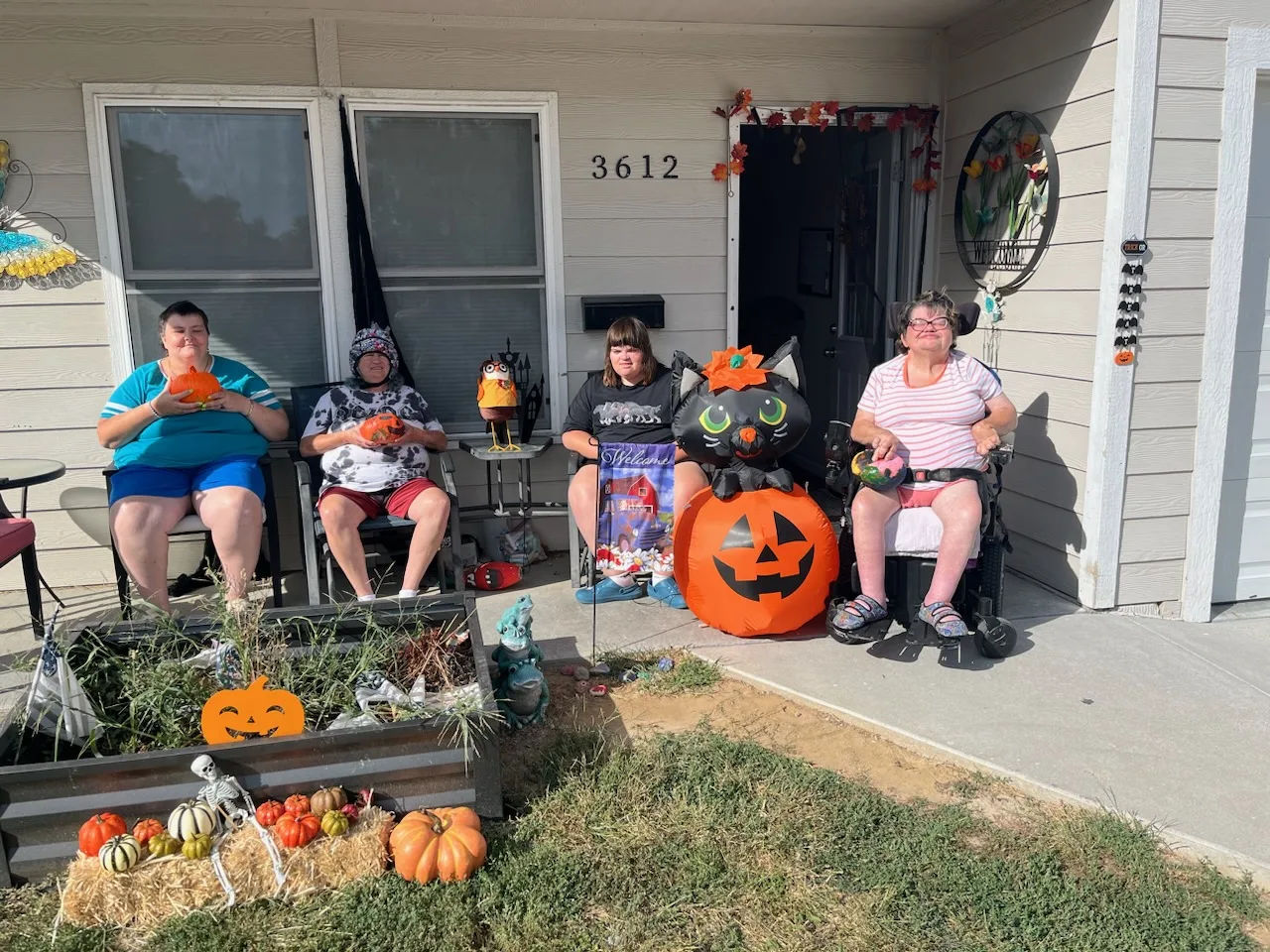 Dawn, Cassie, Rhonda, and Shelby sitting outside their AmeriServe 24-hour residential home, holding painted pumpkins with fall decorations.