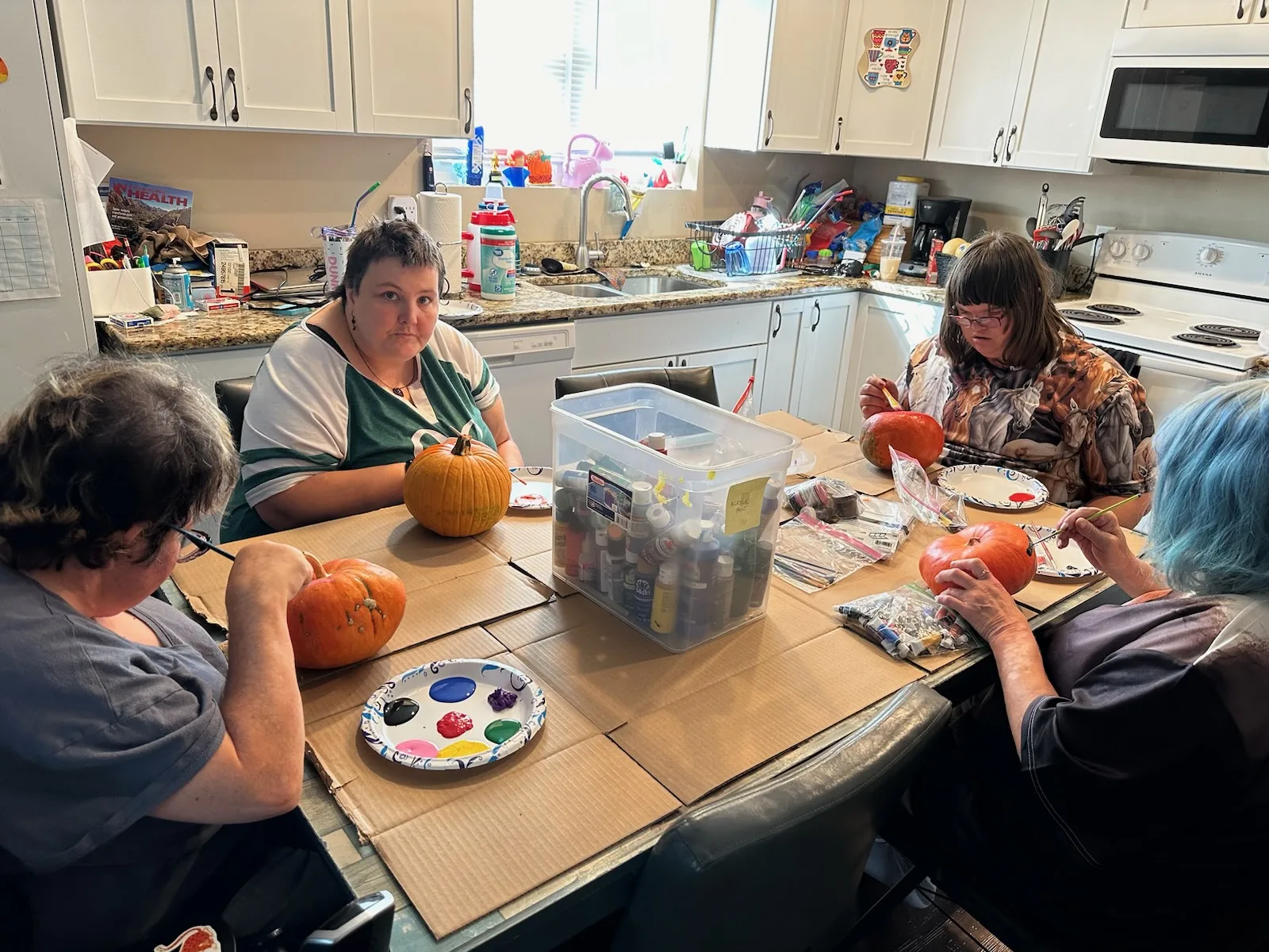 Dawn, Cassie, Rhonda, and Shelby painting pumpkins at their kitchen table in AmeriServe’s 24-hour residential home with their staff's support.