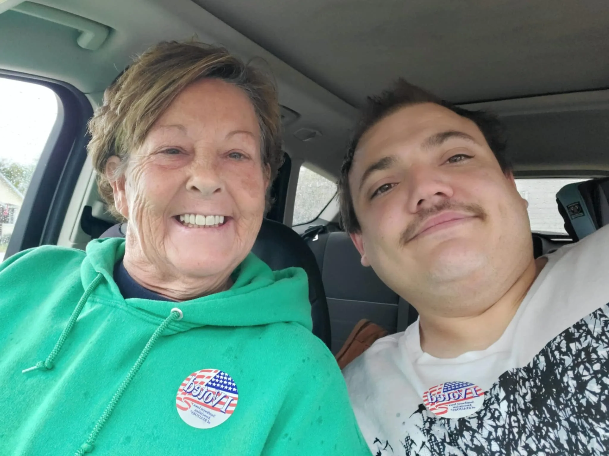 Rhonda and Brian smiling in a car, proudly wearing "I Voted" stickers after participating in the election.